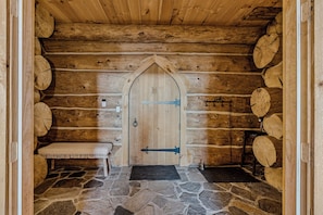 A log cabin interior with a wooden door, stone flooring, and a bench.