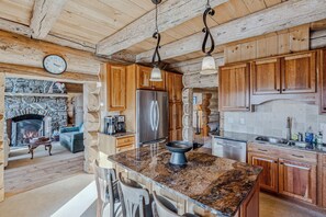 Une cuisine rustique avec des meubles en bois, un comptoir en granit, un réfrigérateur en acier inoxydable et une cheminée en pierre.