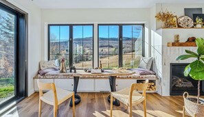 Un espace repas doté d’une grande fenêtre, d’une cheminée et offrant une vue sur un paysage montagneux.