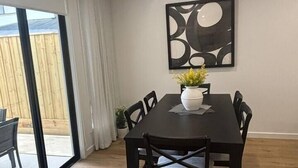 Un coin repas avec une table et des chaises en bois foncé, un vase rempli de fleurs et un tableau abstrait moderne accroché au mur.