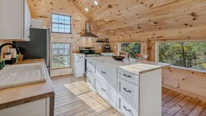 A wooden cabin interior with a kitchen, large windows, and a view of trees. - Reservoir Ridge Loft with Hot Tub & Sauna (Pomfret)