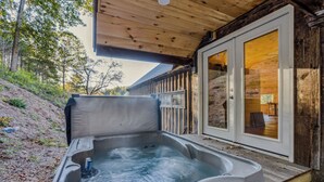 A hot tub with a control panel, a wooden deck, and a glass door leading to an interior room. - Reservoir Ridge Loft with Hot Tub & Sauna (Pomfret)