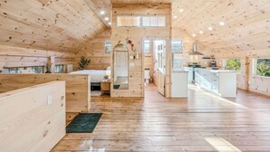 A spacious loft-style room with a high ceiling, wooden floors, a central island with a sink, and a large window providing natural light. - Reservoir Ridge Loft with Hot Tub & Sauna (Pomfret)