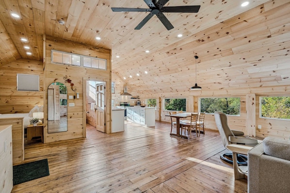 A wooden cabin interior with a dining area, kitchen, and a ceiling fan.