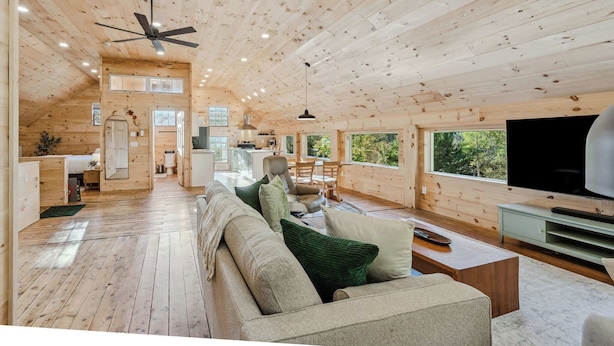 A spacious cabin interior with wooden walls, a ceiling fan, a dining area, and a TV. - Reservoir Ridge Loft with Hot Tub & Sauna (Pomfret)