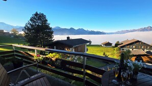 Ein Balkon mit Holzbalkon, der auf eine gebirgige Landschaft mit Häusern und einem klaren Himmel blickt.