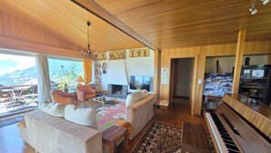 A spacious living room with a wooden ceiling, a sofa, a coffee table, a piano, and a fireplace. - Alegria Beatenberg (Beatenberg)