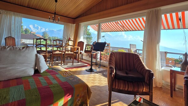 Ein gemütliches Zimmer mit einem Bett, Holzboden, einem Esstisch mit Stühlen und Bergblick durch große Fenster.