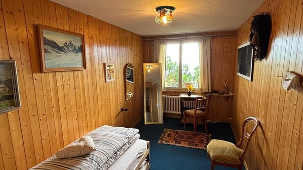 A room with wooden walls, a bed, a desk, a chair, and a window. - Alegria Beatenberg (Beatenberg)