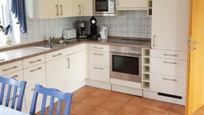 A kitchen with white cabinets, a microwave, a stove, and a sink. There is a blue table with chairs. - House Kiki in Dornumersiel (Dornum)