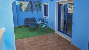 A blue-walled patio with a tiled floor, a metal bench, a small table, and a chair. - Apartamentos Blue Suites Alicante (Alicante)
