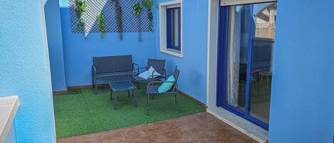 A blue-walled patio with a tiled floor, a metal bench, a small table, and a chair.