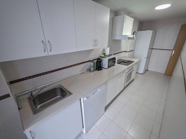 A modern kitchen with white cabinets, a stainless steel sink, a built-in microwave, and a stove.