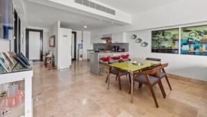 A modern kitchen with a central island, red bar stools, and a dining table with chairs.