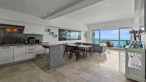A modern kitchen with a dining area, large windows, and a view of the ocean.