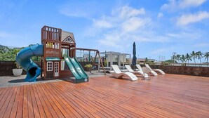 A wooden deck with a slide, lounge chairs, and a view of the city skyline.
