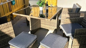 Een terras buiten met rieten meubilair, een tafel met glazen blad en een potplant.
