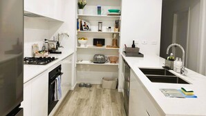 Een moderne keuken met witte kastjes, een inbouwoven, een spoelbak en een compact opbergruimte met planken en een kleine koelkast.