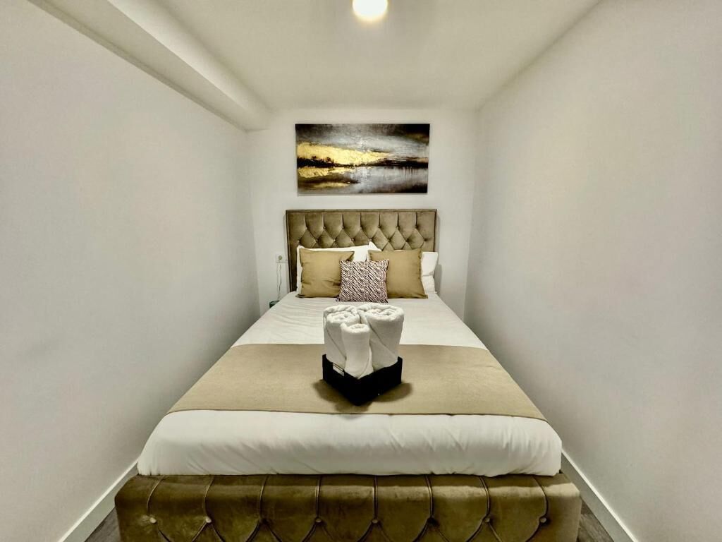 A hotel room with a bed, a headboard, a painting on the wall, and a set of towels on the bed.