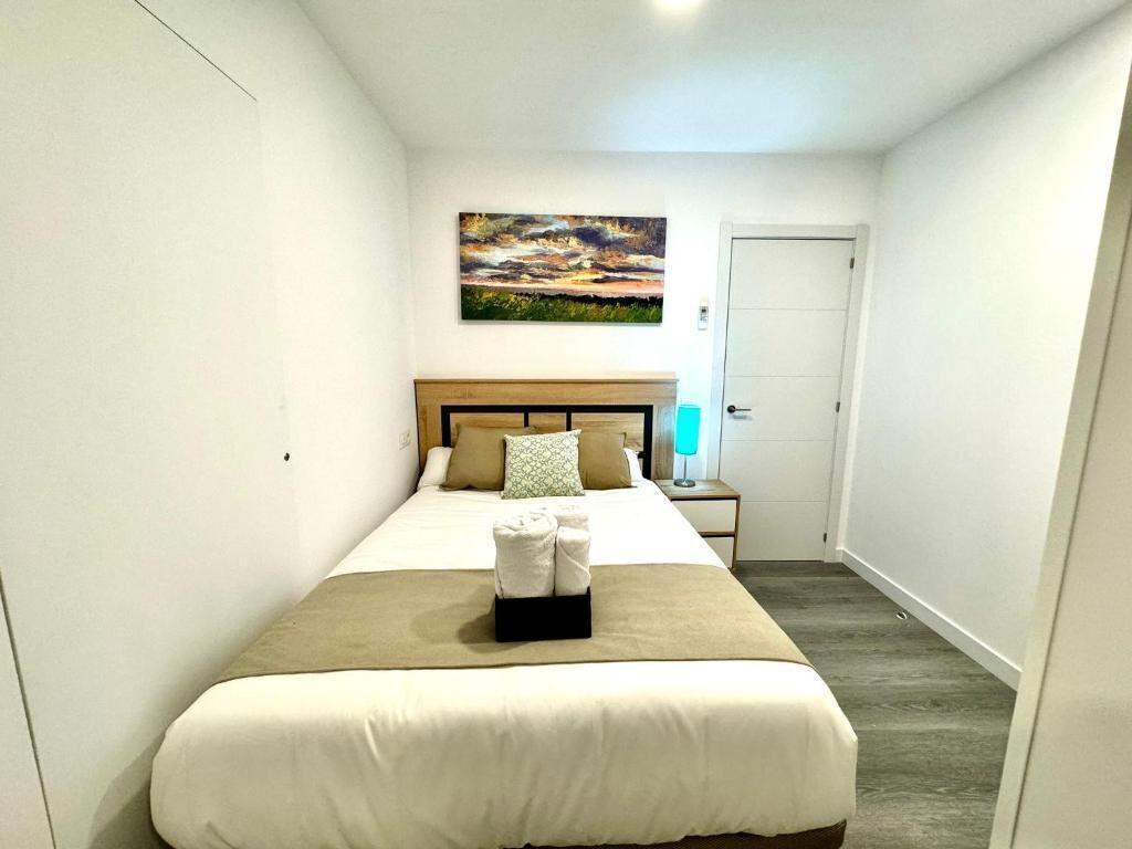 Ein Hotelzimmer mit Bett, einem Bild an der Wand, einer Tür und einem Nachttisch mit Lampe.