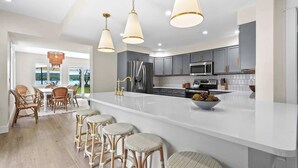Una cocina moderna con gabinetes grises, electrodomésticos de acero inoxidable, una isla grande con taburetes e iluminación colgante.