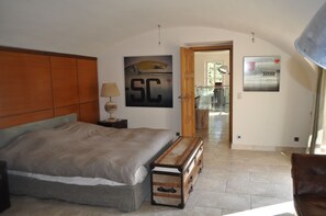 A bedroom with a large bed, a wooden headboard, a bench, and a door leading to a bathroom. - Saint-Tropez center on foot – Villa 5★, 5 suites, pool & garden – 10 pers. (Saint-Tropez)