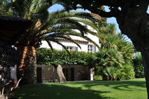 A white building with a tiled roof, surrounded by lush greenery and palm trees. - Character villa in the heart of St-Tropez! Swimming pool, lush garden and calm (Saint-Tropez)