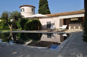 Ein Schwimmbad mit einer Springbrunnenanlage, umgeben von einer Terrasse mit Liegestühlen und einer Pergola.