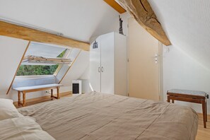 A bedroom with a sloped ceiling, a skylight, a bed, a wardrobe, and a small table. - Gîte Mélany for 4 Guests (Chargé)