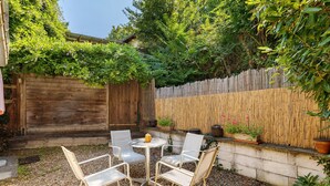 Eine Terrasse mit einem runden Tisch und vier Stühlen, umgeben von einem Holzzaun und üppiger Bepflanzung.