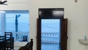 Una habitación con un banco de madera, un ventilador de techo, un ventanal con vista al mar y una puerta que da a un balcón.
