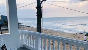 Un balcón con barandilla blanca, una silla negra y vista a la playa y al océano.