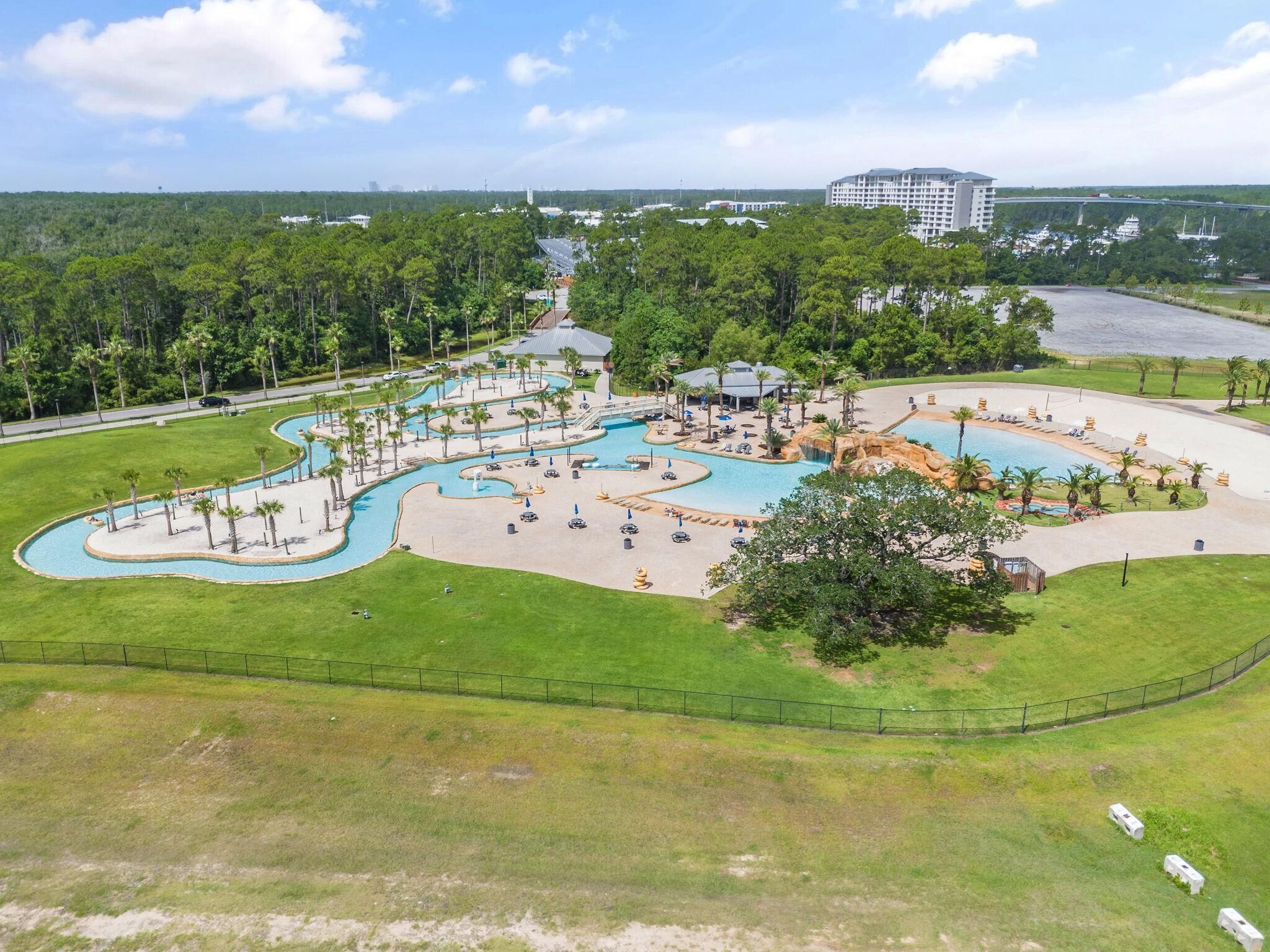 Vue aérienne d’un complexe hôtelier doté d’une grande piscine, de palmiers et d’un pont en arrière-plan.