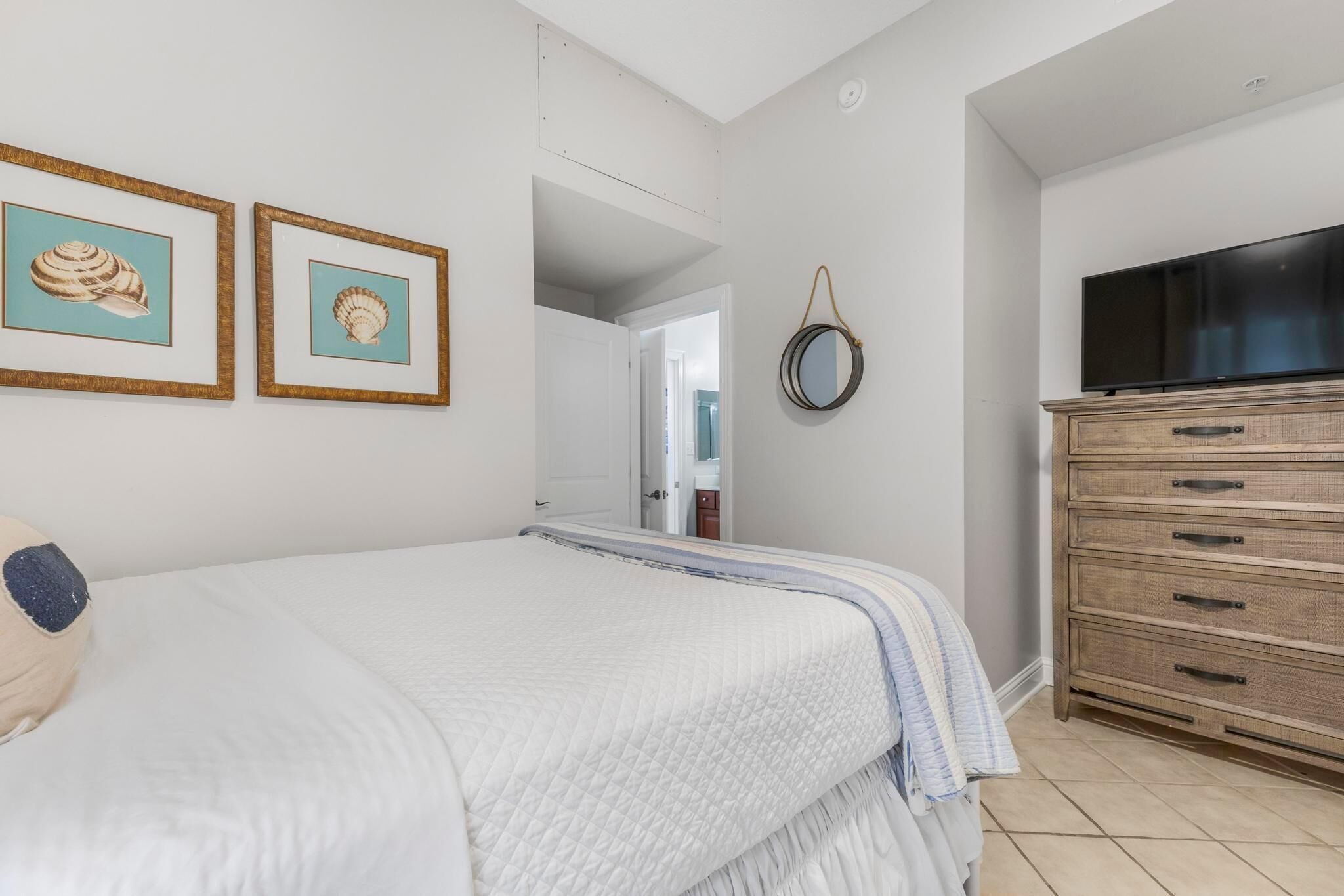 Un dormitorio con cama, cómoda, televisor y dos cuadros en la pared.