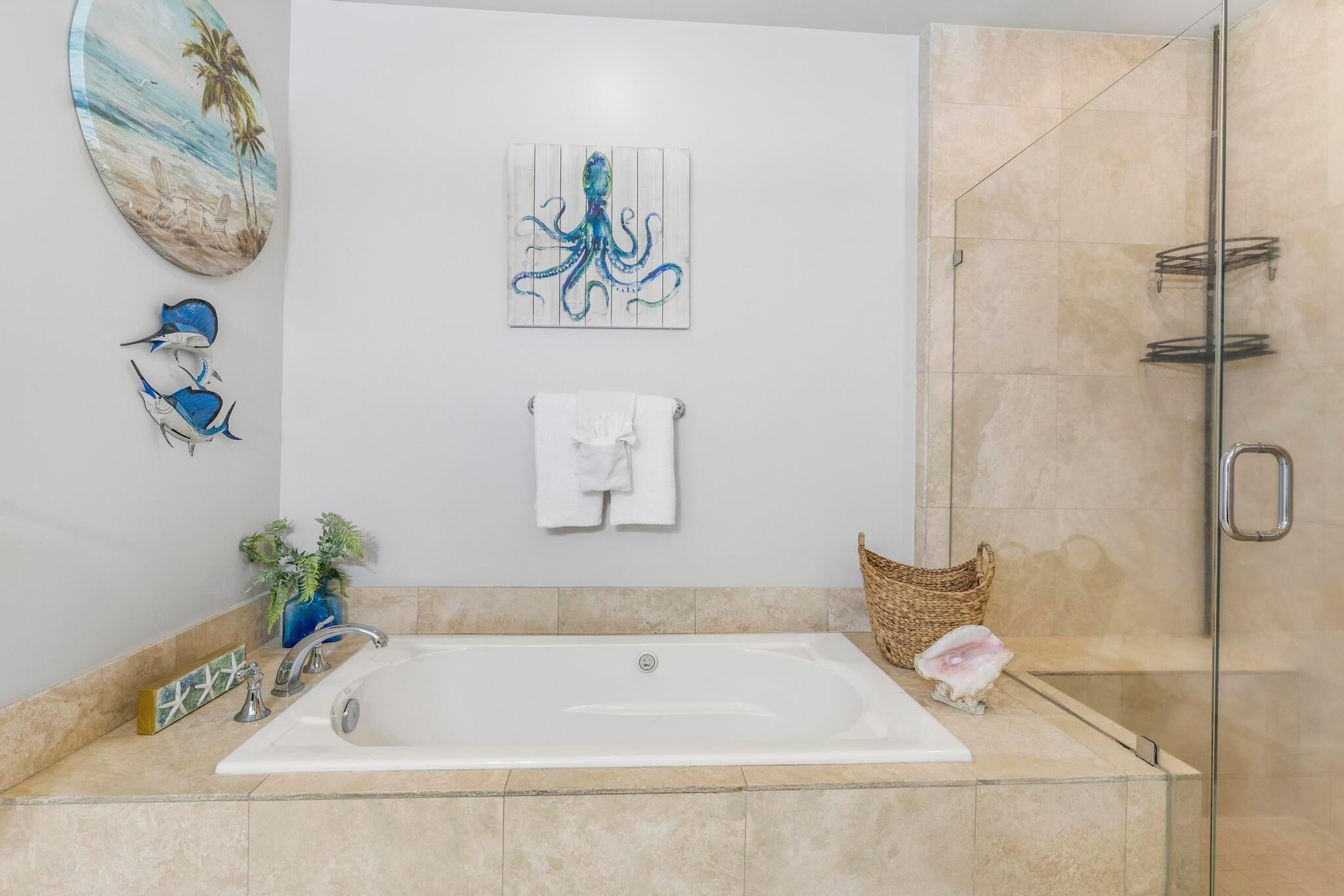 A modern bathroom with a large bathtub, a glass shower enclosure, and decorative wall art including a beach scene and an octopus.