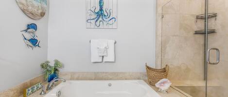 A modern bathroom with a large bathtub, a glass shower enclosure, and decorative wall art including a beach scene and an octopus.