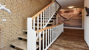 A staircase with a wooden handrail and white balusters, leading to a room with a brick wall and a large seagull mural. - Ferienwohnung in Bensersiel, 300 m vom Strand (Bensersiel)