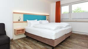 A hotel room with a bed, a nightstand, a chair, and a window with blinds. - Ferienwohnung in Bensersiel, 300 m vom Strand (Bensersiel)