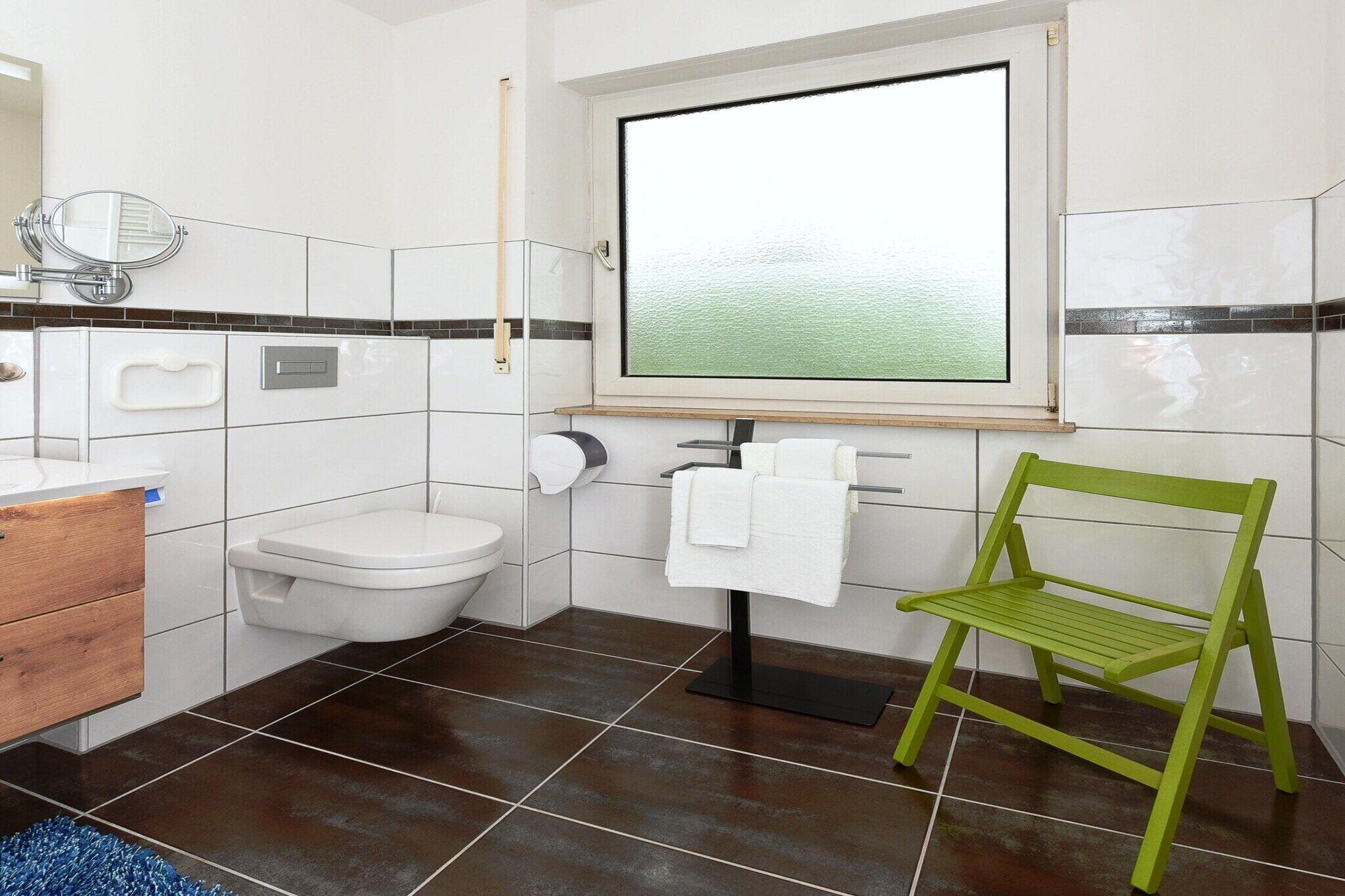 Un baño con inodoro, lavabo, espejo y una silla verde.
