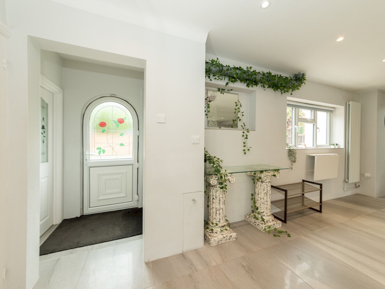 Ein modernes Interieur mit einer weißen Tür, einer Glastür mit floralem Dekor, einem Glastischchen mit verzierten Säulen und einem Heizkörper.
