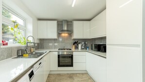 A modern kitchen with white cabinets, a stainless steel range hood, a built-in oven, and a dishwasher. - Pass the Keys | Bright House with Smart TV & Home Comforts (Reading)