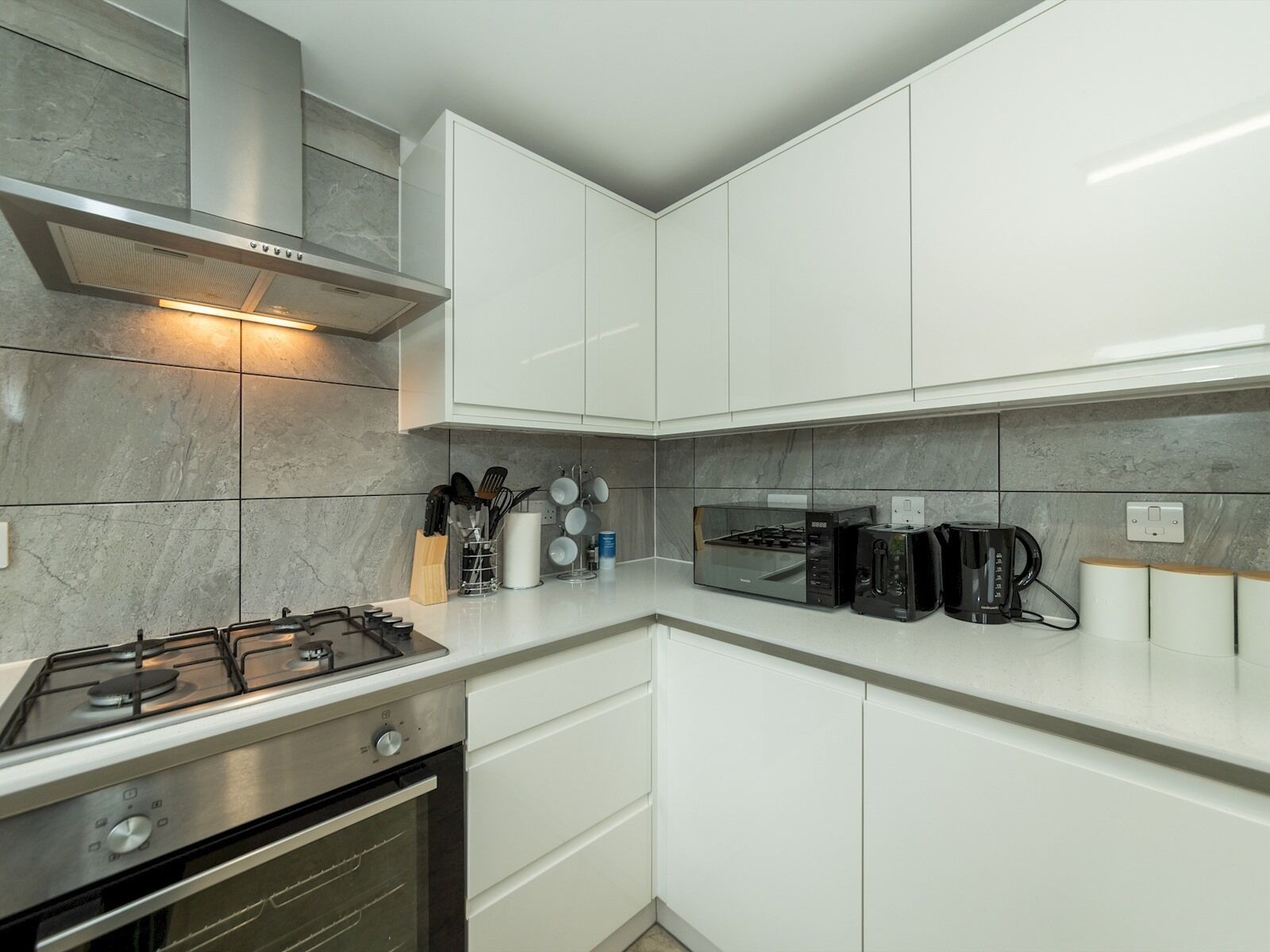 Una cucina moderna con mobili bianchi, una cappa aspirante in acciaio inossidabile, un fornello a gas, un forno integrato e una macchina per il caffè.