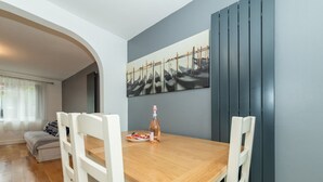 A dining area with a wooden table and white chairs, a painting of boats on the wall, and a bottle of wine on the table. - Pass the Keys | Bright House with Smart TV & Home Comforts (Reading)