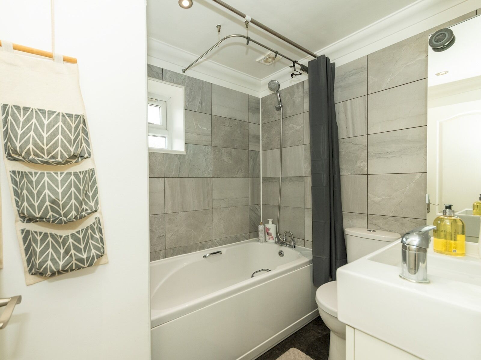 Une salle de bain moderne avec une baignoire sur pieds, une douche et des toilettes. Trois coussins à motifs sont accrochés au mur, et des articles de toilette sont disposés sur le comptoir.