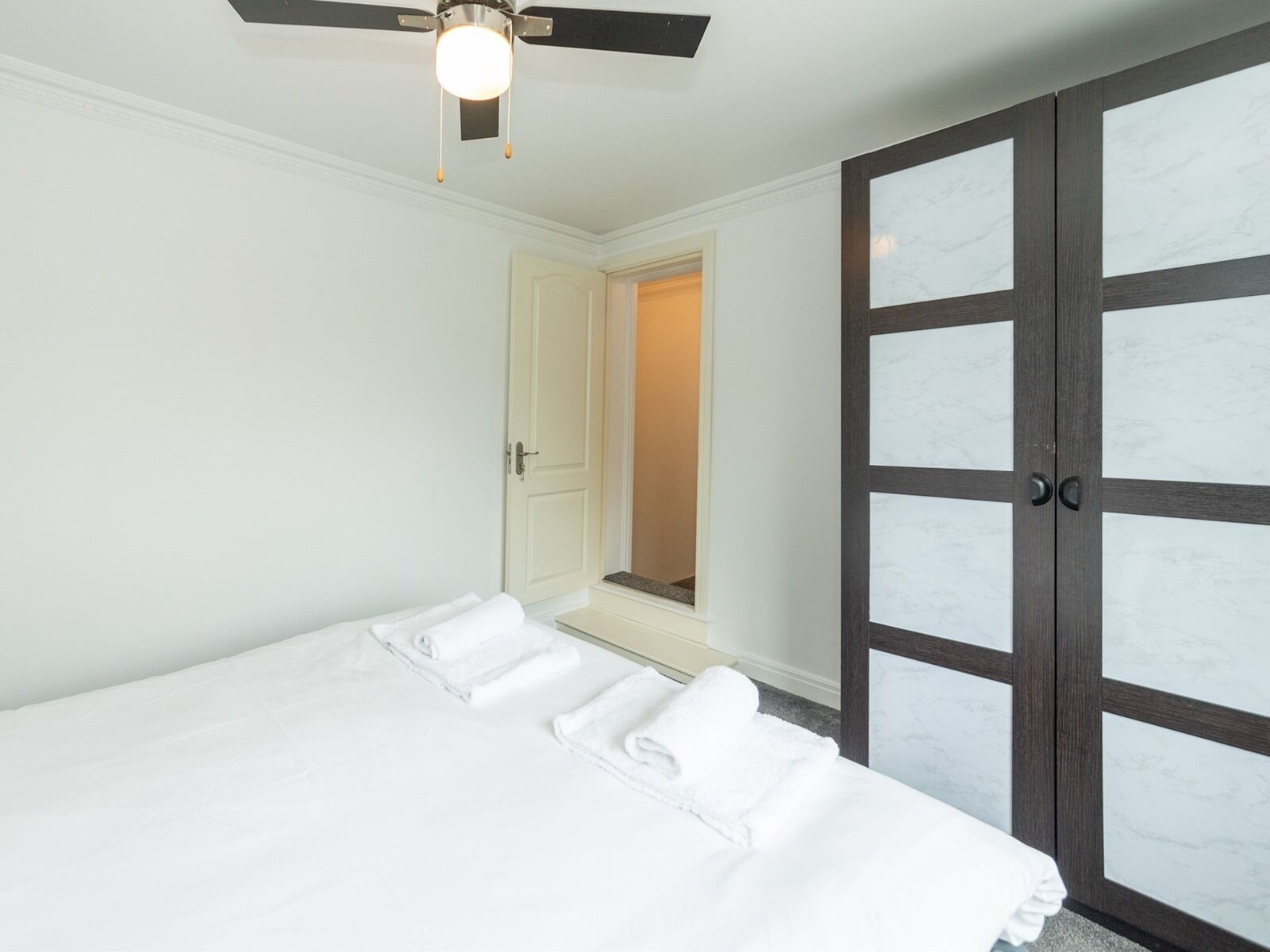 Een hotelkamer met een bed, een plafondventilator en een garderobe met geëtste glazen deuren.