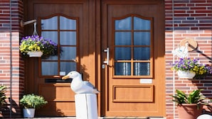 A wooden double door with a number '2' above it, a mailbox, and a bird statue on a post. - Ferienwohnung mittendrin in Bensersiel (Bensersiel)
