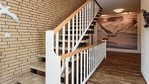 Eine Treppe mit Holzsitzen und weißen Geländern, die zu einer Zwischenebene führt, auf der eine Vogel-Skulptur angebracht ist.