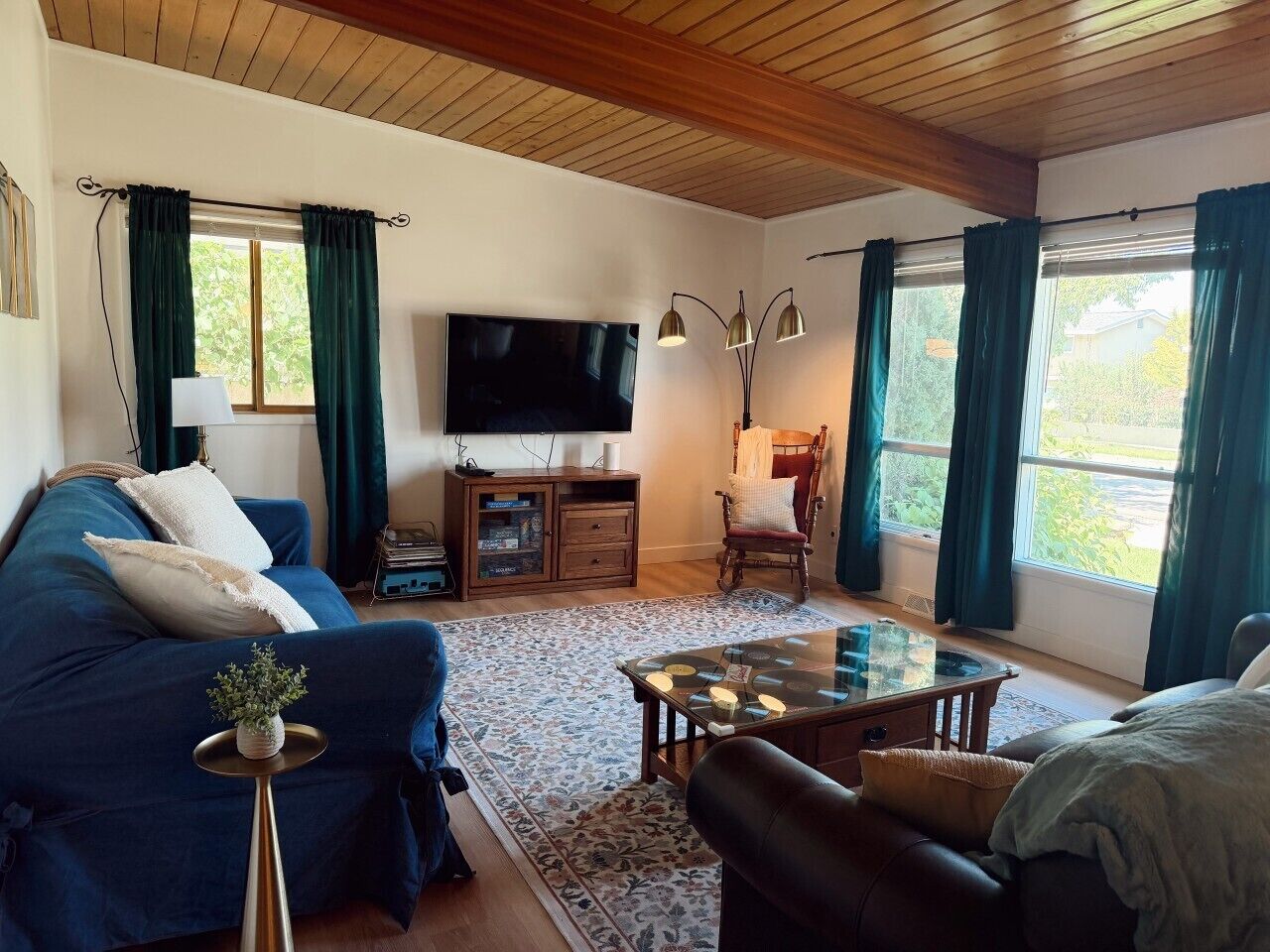 Un salon avec un canapé bleu, un téléviseur, un plafond en bois et une fenêtre avec des rideaux.