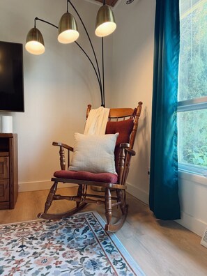 A wooden rocking chair with cushions, a patterned rug, and a television on the wall.