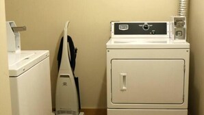 Une buanderie équipée d’un lave-linge et d’un sèche-linge à chargement frontal, d’un aspirateur et d’un meuble de rangement.